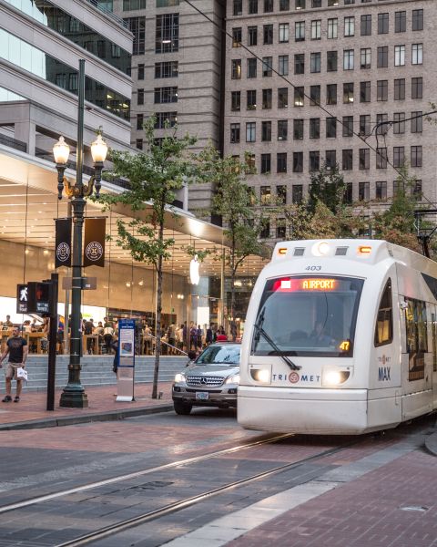 A light rail train passes in front of a modern, glass-encased retail store