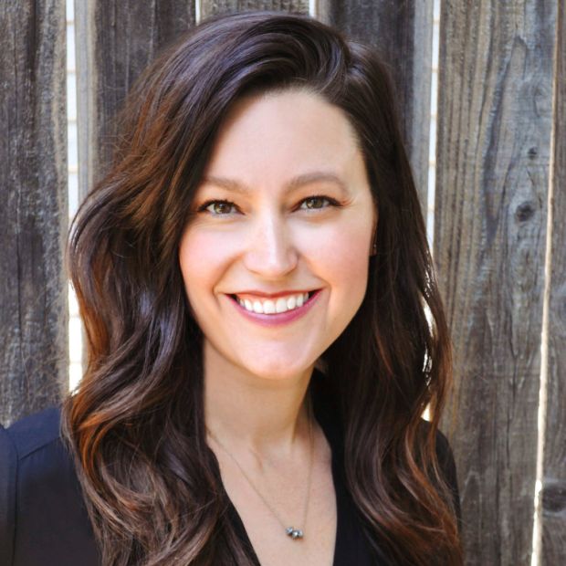 a smiling woman with long brown hair in front of fence boards