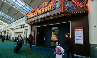 travelers walk past a small movie theater located within an airport