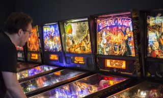 a man playing pinball in a row of other brightly lit pinball machines