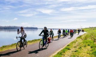 a crowd of bikers with Friends on Bikes ride a path along a river
