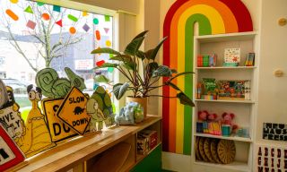 a rainbow frames a bookcase filled with children's books and toy, a colorful window display has animal signs and stuffed animals