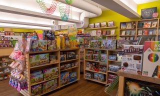 wooden shelves in a bright store filled with games, toys, puzzles, a rainbow slinky hangs from the ceiling
