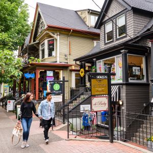 two people walking on a sidewalk in front of boutique shops in old Victorian homes