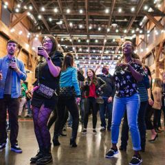 young people stand with drinks in their hands, string lights above in chic venue