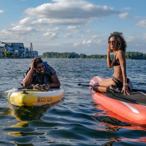two women on paddleboards in a river with houseboats in the distance
