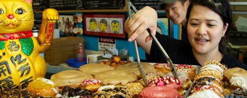 person using tongs to select a doughnut from a tray