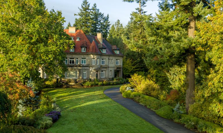 A large stone mansion with red roof surrounded by trees