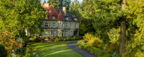 A large stone mansion with red roof surrounded by trees