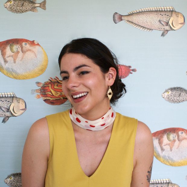 a woman in a yellow top and scarf in front of a wall with pictures of fish on it