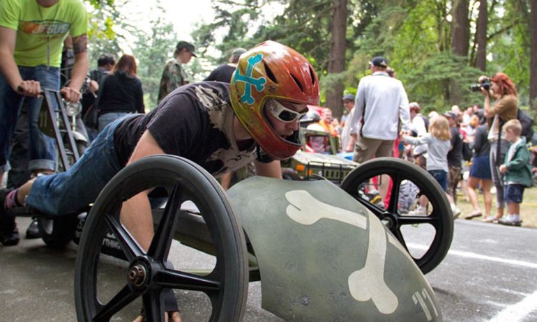 an adult prepares to race a skull and crossbones-styled soapbox