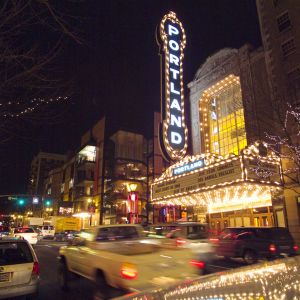 The iconic Portland sign lights up the night as cars stream past the Arlene Schnitzer Concert Hall.