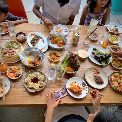people sit around a vast spread of Korean food arrayed on a wooden table