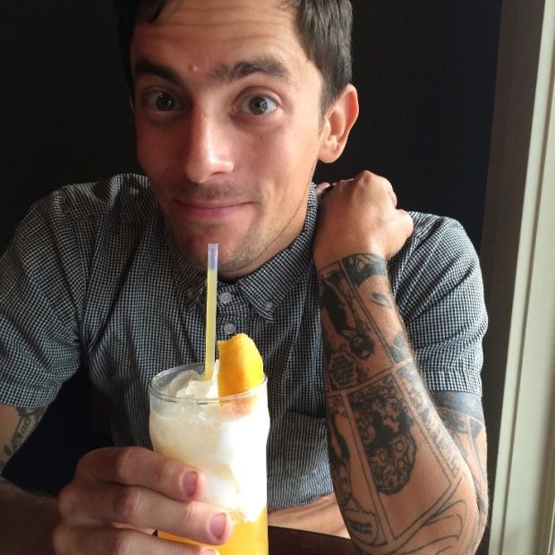 a man holding a fruity drink with tattoos on his arms