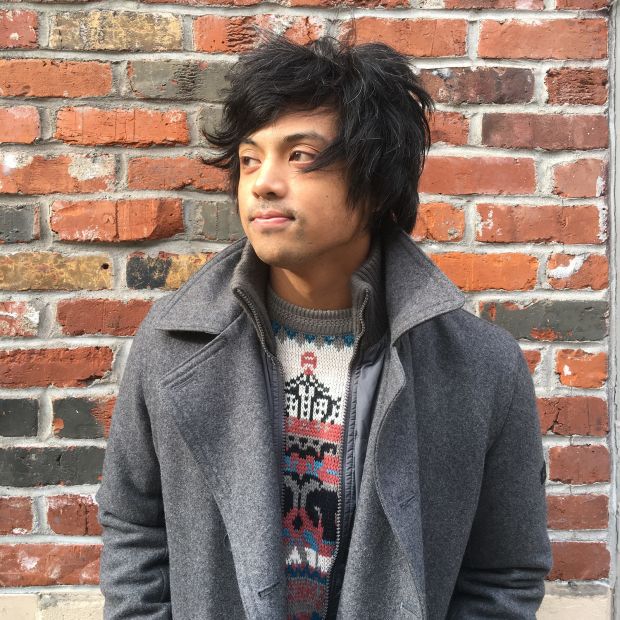 a man in a grey coat standing in front of a brick wall