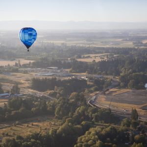 A hot air balloon floats above a wooded valley.
