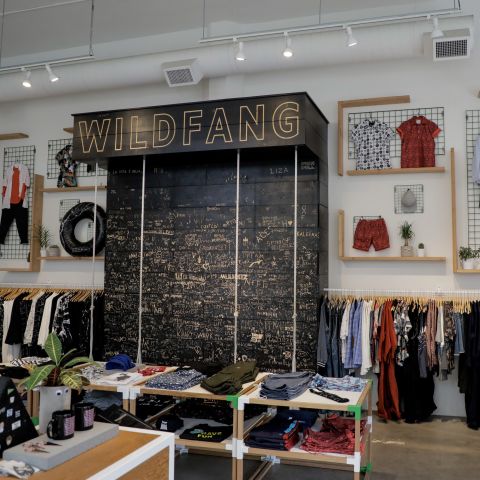 clothing on racks and folded on tables and large display with handwritten words