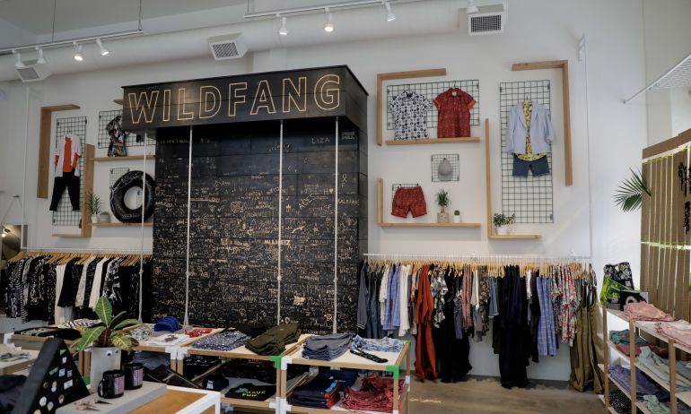clothing on racks and folded on tables and large display with handwritten words