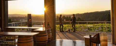 people stand on a patio sipping wine with a view of the valley as the sun sets