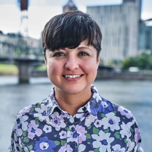 a close-up of a person in a floral print shirt standing in front of a river