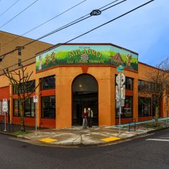 a couple stands in front of a large theater painted orange with a sign reading “En Centro Milagro”