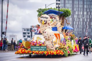 large float made of roses and flowers on a bridge with people waving from the float to onlookers
