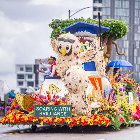 large float made of roses and flowers on a bridge with people waving from the float to onlookers