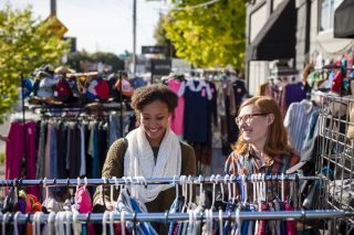 two people look through outdoor racks of clothing on a sunny day