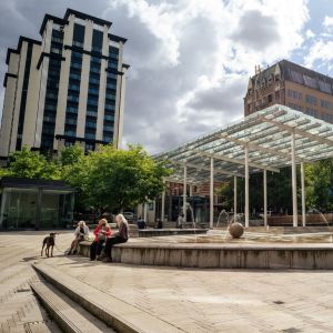 people sit on the edge of a fountain in a spacious urban park