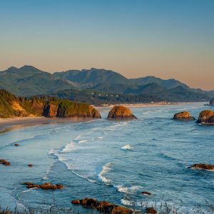 an aerial view of the Oregon Coast with the coast mountain range in the background, a sea of green