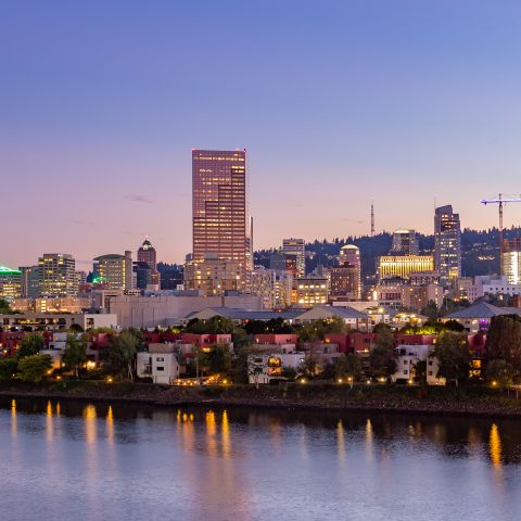 nighttime falls on a city, as sun sets city lights reflect on the river