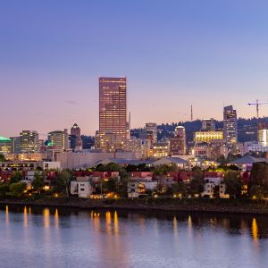 nighttime falls on a city, as sun sets city lights reflect on the river