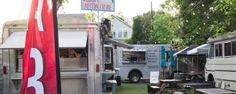 A food cart pod with food trucks gathered around a small seating area with picnic tables.