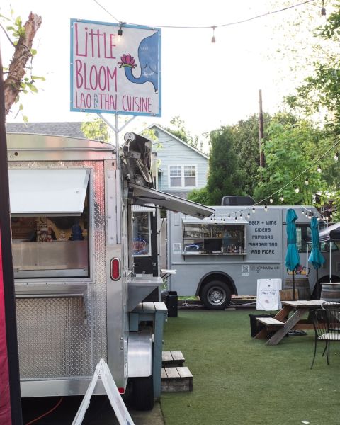 A food cart pod with food trucks gathered around a small seating area with picnic tables.
