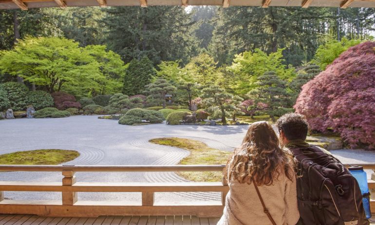 A couple sits viewing a serene flat rock garden surrounded by trees and shrubs.