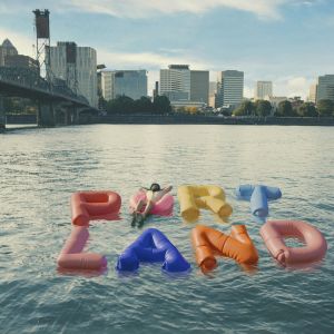 stylized photo showing PORTLAND spelled out in inflatable floaties on the water with a person floating on the \'O\' floatie