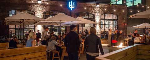 a crowd of people eat, drink and converse on an expansive, warmly lit patio at night