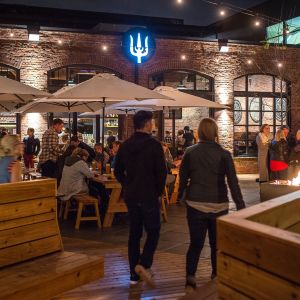 a crowd of people eat, drink and converse on an expansive, warmly lit patio at night