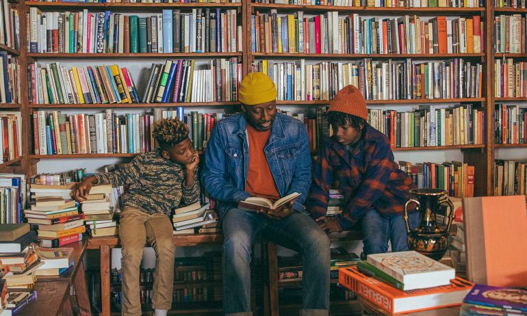 Three people sit and read a book at Mother Foucault\'s bookstore in front of a wall of books.