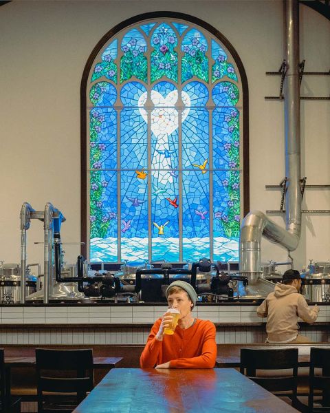 a person sips a beer in front of a stained glass window