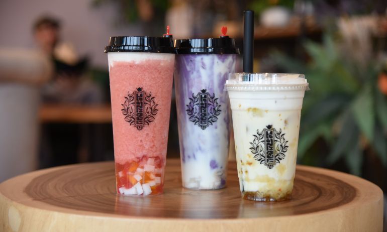 Three cups of flavored boba tea rest on small wooden table.