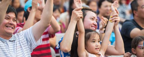 a family sitting in chairs raise their arms while watching a performance