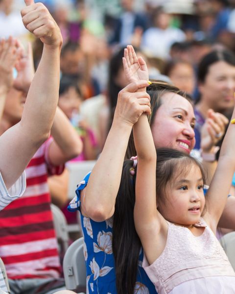 a family sitting in chairs raise their arms while watching a performance