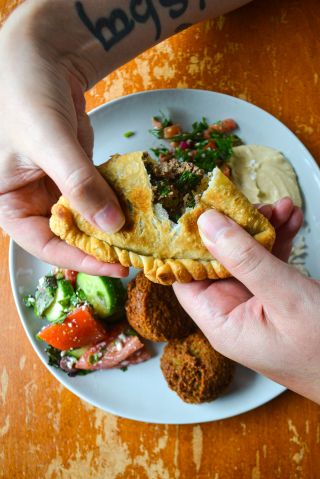 two hands pull apart a savory pastry over a plate of food