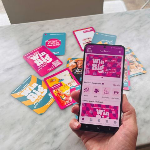 a hand holds a phone displaying an app that says “Win Big” over a pile of colorful trading cards and promotional materials