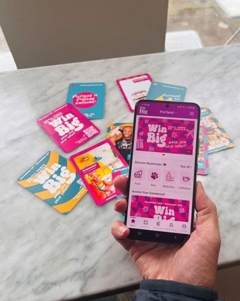a hand holds a phone displaying an app that says “Win Big” over a pile of colorful trading cards and promotional materials