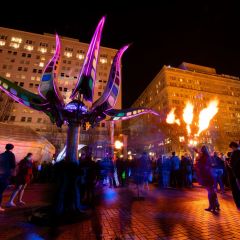 a crowd mingles under a fire display and a lighted purple sculpture