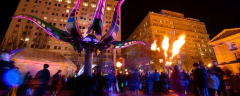 a crowd mingles under a fire display and a lighted purple sculpture