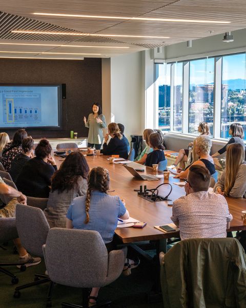 a large group of people around a conference room table watch a person giving a presentation