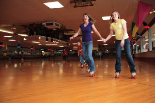 two people smile while holding hands and skating across a classic wooden roller rink